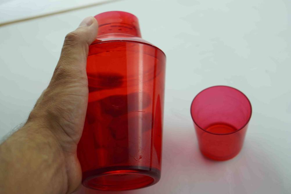 Cocktail-Shaker im Test: Eine Hand hält einen Shaker vor eine helle Fläche, neben einem roten Glas