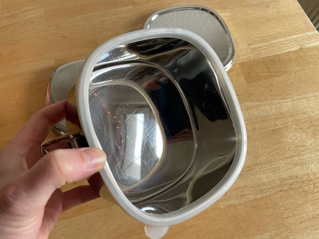 Eine Hand hält die getestete Metallbrotdose inklusive Dichtungsring über einem Holztisch.