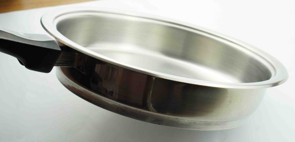 Edelstahlpfanne getestet: Eine Hand hält eine Pfanne leicht schräg auf einer hellen Oberfläche