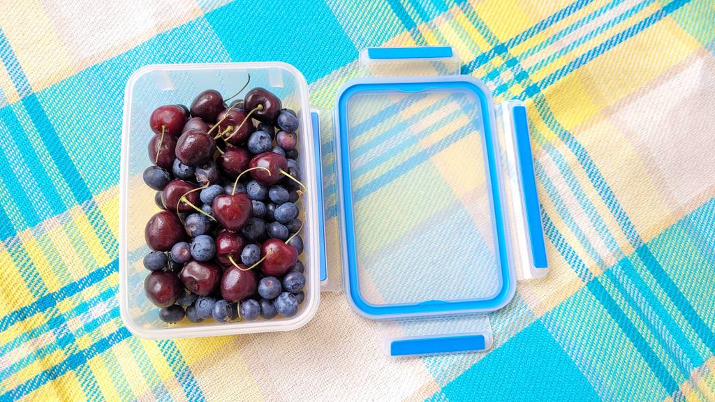 Geöffnete Frischhaltedose mit Heidelbeeren und Kirschen - Deckel neben liegend.