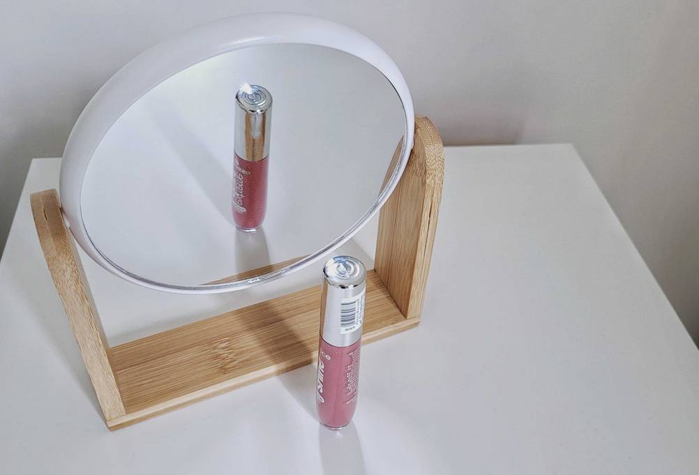 Getester Lipgloss vor einem Kosmetikspiegel.