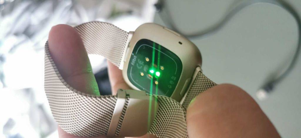 Fitbit im Test: Rückseite einer goldenen Fitbit-Uhr, auf der ein grünes Licht leuchtet.