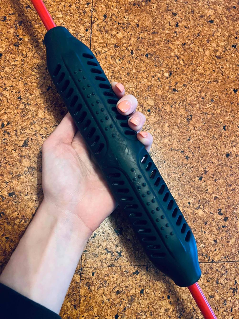 Fitness Schwingstab getestet: Eine Hand hält das Mittelstück vor eine Holzfläche.