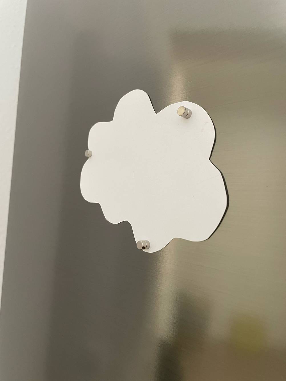 Ein Blatt Papier wird mit den getesteten Kühlschrankmagneten an einem Kühlschrank befestigt.