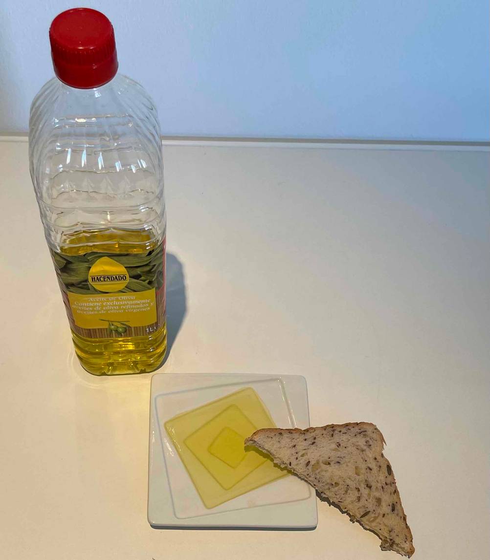 Spanisches-Olivenöl im Test: ein spanisches-Olivenöl in einer Plastikflasche steht neben einem Teller und einem Stück Brot.