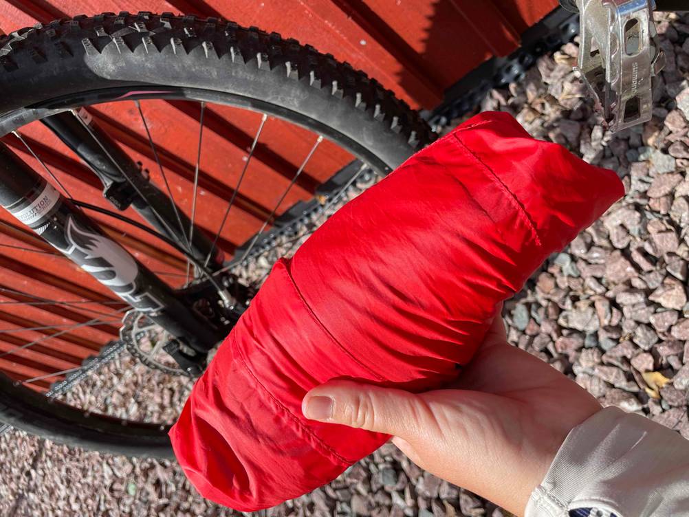 Fahrradjacke getestet: Eine Hand hält ein eingerolltes Produkt vor ein Fahrrad.