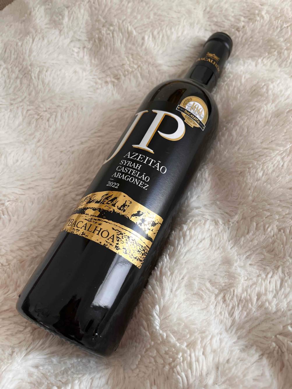 Eine getestete Flasche Rotwein (lieblich) von schräg unten auf einem hellen Fell liegend.