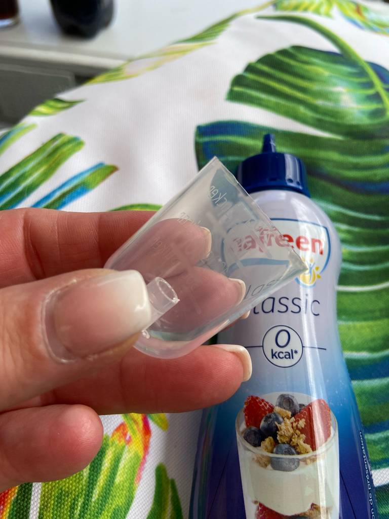 Der getestete flüssige Süßstoff in der Kunststoffflasche liegt hinter dem Messbecher, der von einer Hand gehalten wird.