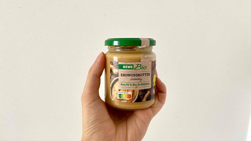 Erdnussbutter getestet: Eine Hand hält ein Glas vor eine helle Wand.