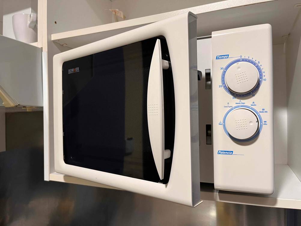 Mikrowelle ohne Grill im Test: Das Gerät von vorne mit leicht geöffneter Tür in einem weißen Regal