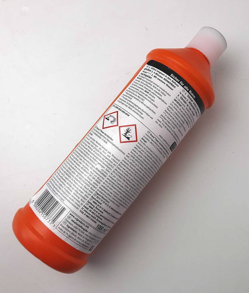Die getestete Rohrreinigung in der orangefarbenen Kunststoffflasche liegt auf einer weißen Fläche.