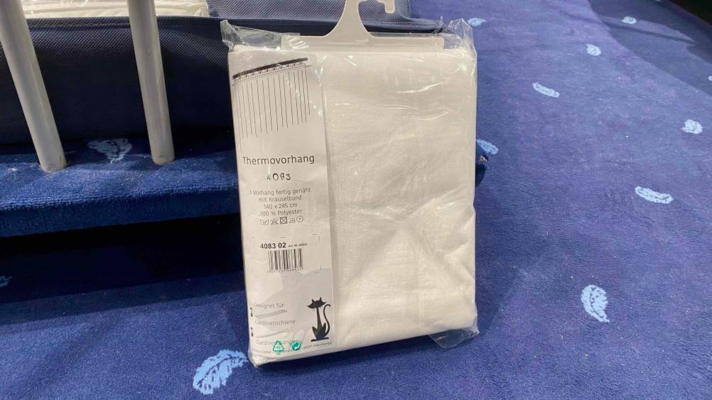 Thermovorhang im Test: ein weißer Thermovorhang ist in Verpackung auf einem blauen Tepppich platziert.
