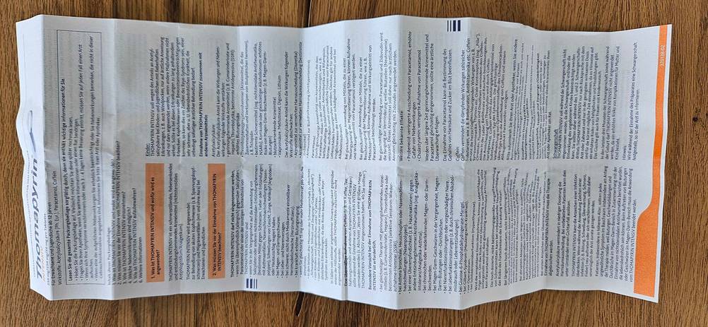Migräne-Tabletten getestet: Beipackzettel entfaltet auf einer Holzoberfläche.