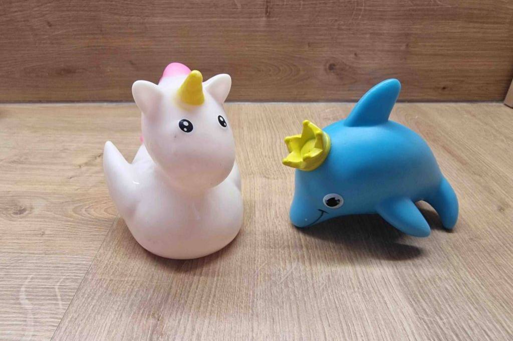 Wasserspielzeug im Test: eine Einhorn-Badefigur und eine Delfin-Badefigur, stehen auf einer Holzfläche.