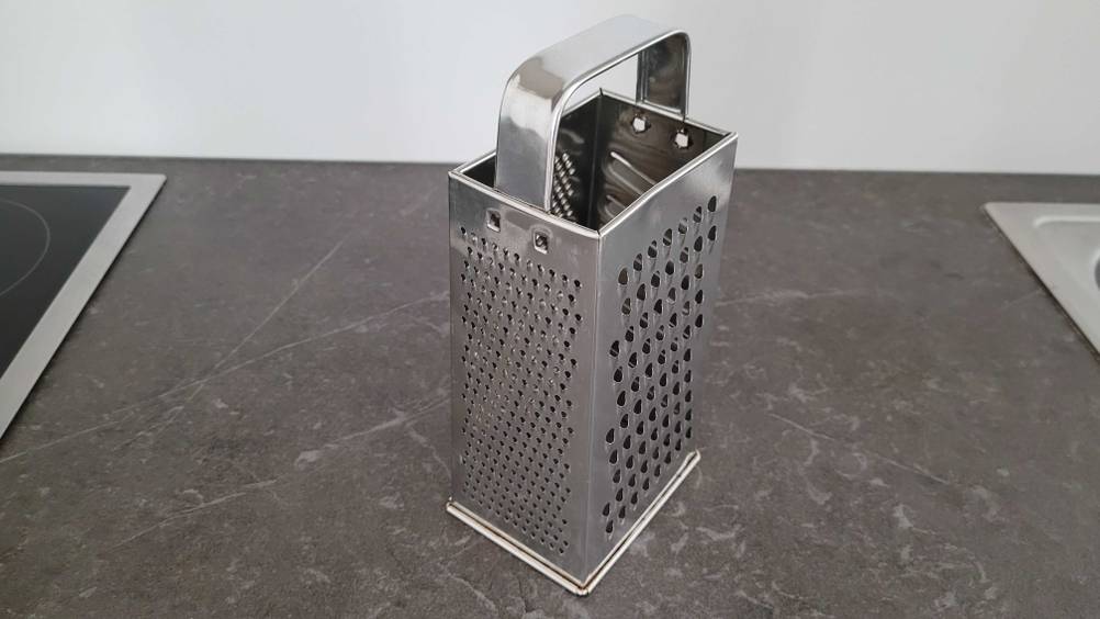 Eine getestete Käsereibe steht leicht seitlich auf einer dunklen Oberfläche.