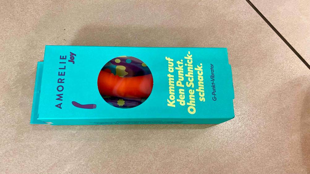 Vibrator getestet: die Verpackung mit orangefarbigem Vibrator drin ersichtlich ist auf einem Boden platziert.