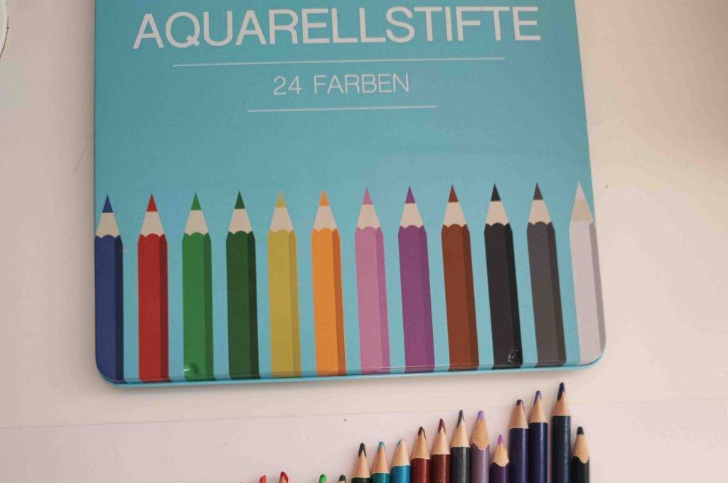 Aquarellstifte getestet: Vor ihrer Box liegen mehrere Aquarellstifte farblich sortiert.