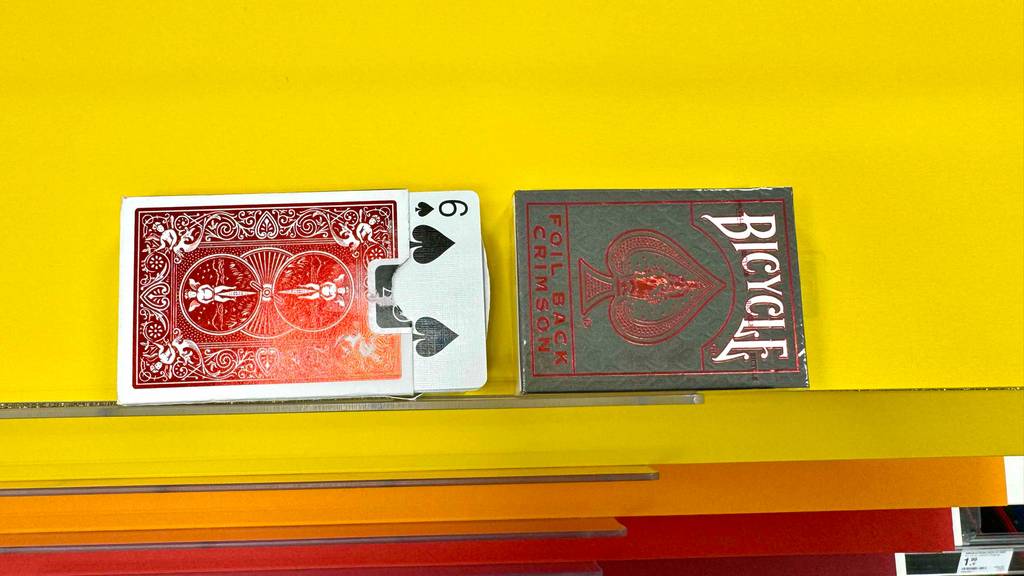 Zwei Packungen getestete Pokerkarten liegen auf einer gelben Fläche, wobei eine Packung geöffnet und ein paar Karten herausragen.