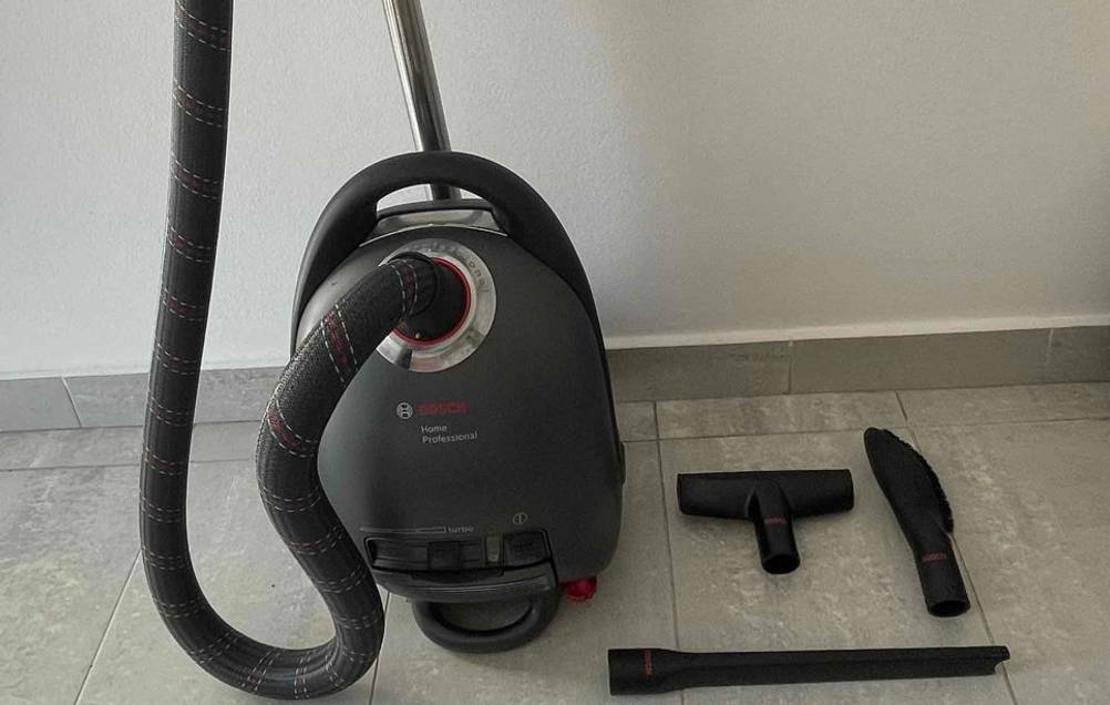 Der Staubsauger und Zubehörbürsten stehen auf einem Fliesenboden vor einer hellen Wand.