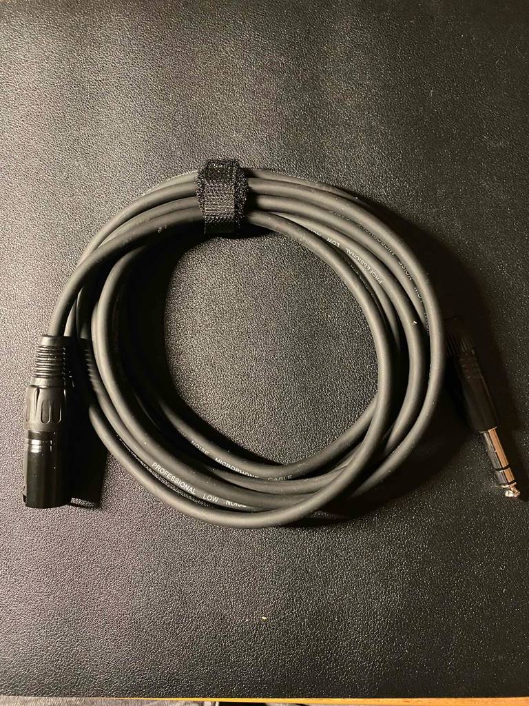 Ein getestetes, zusammengebundenes XLR-Kabel auf einer schwarzen Fläche liegend.