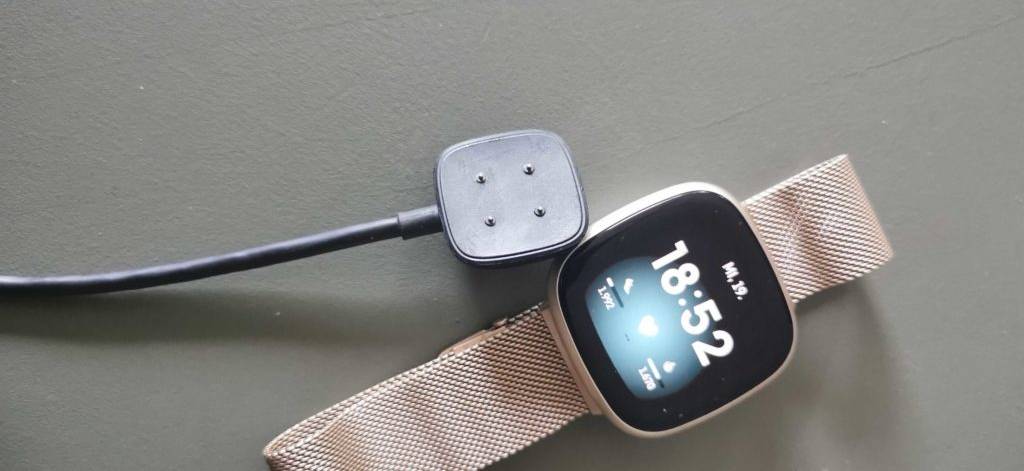 Getestete Fitbit liegt neben einem Fitbit-Ladegerät auf einem weißen Tisch.