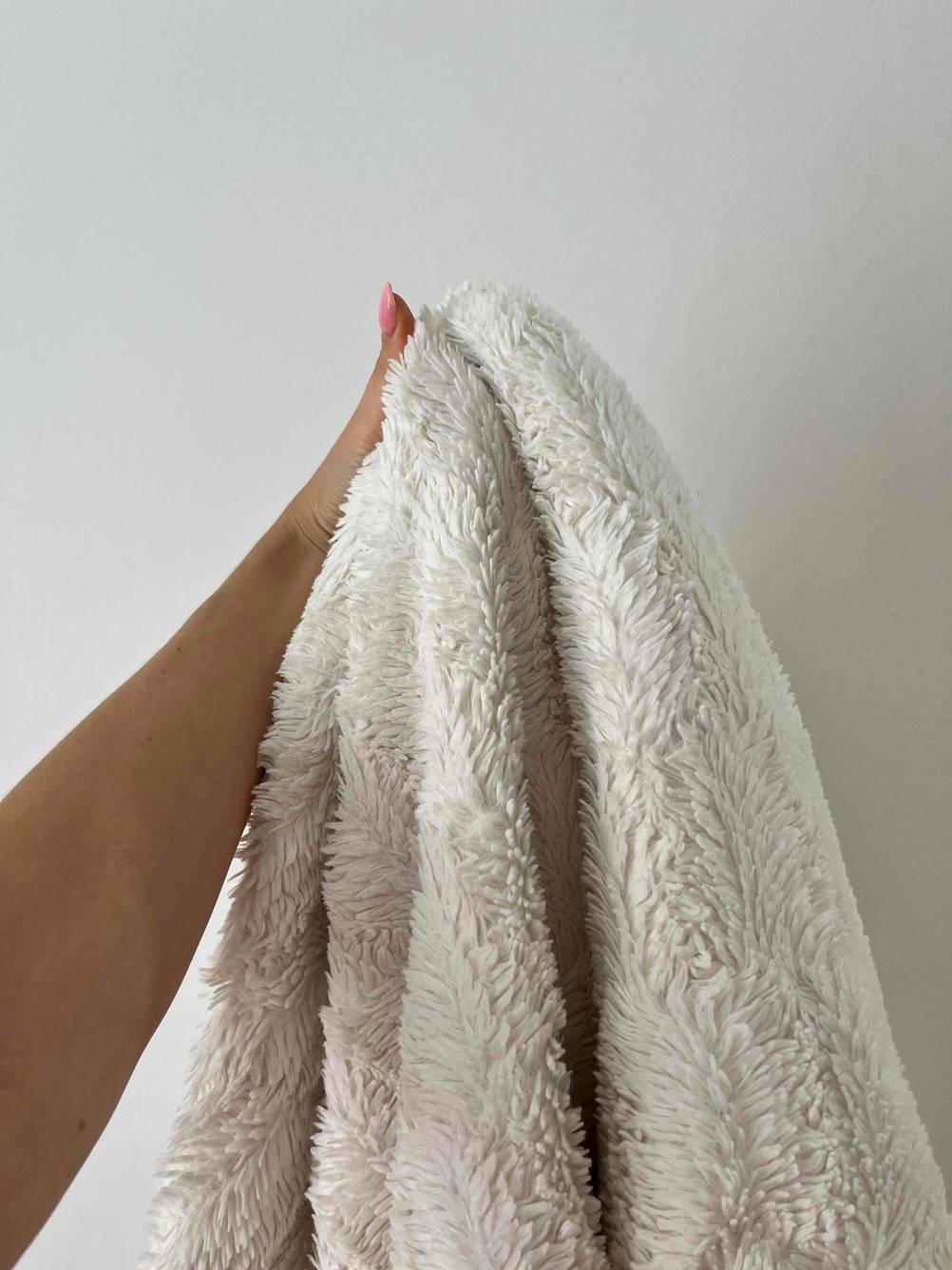 Eine Hand hält die getestete Kuscheldecke hoch vor eine helle Wand.
