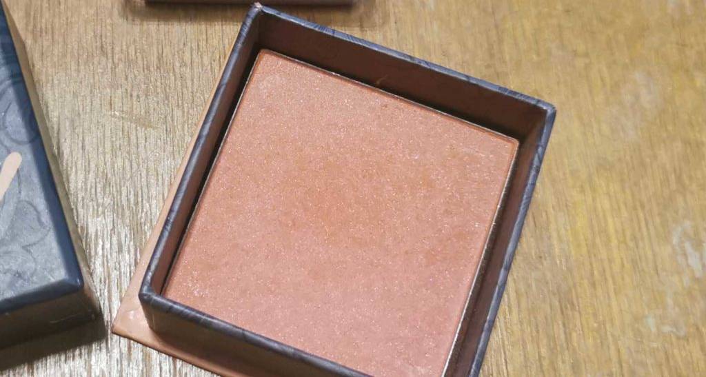 Geöffnetes Rouge auf einem Tisch mit dazu passendem Pinsel.