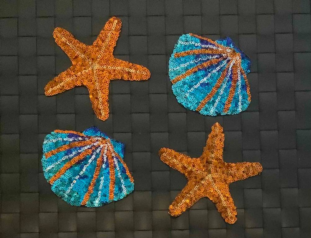 Auf einer dunklen Fläche liegen mehrere getestete Patches, hier Muscheln und Seesterne.