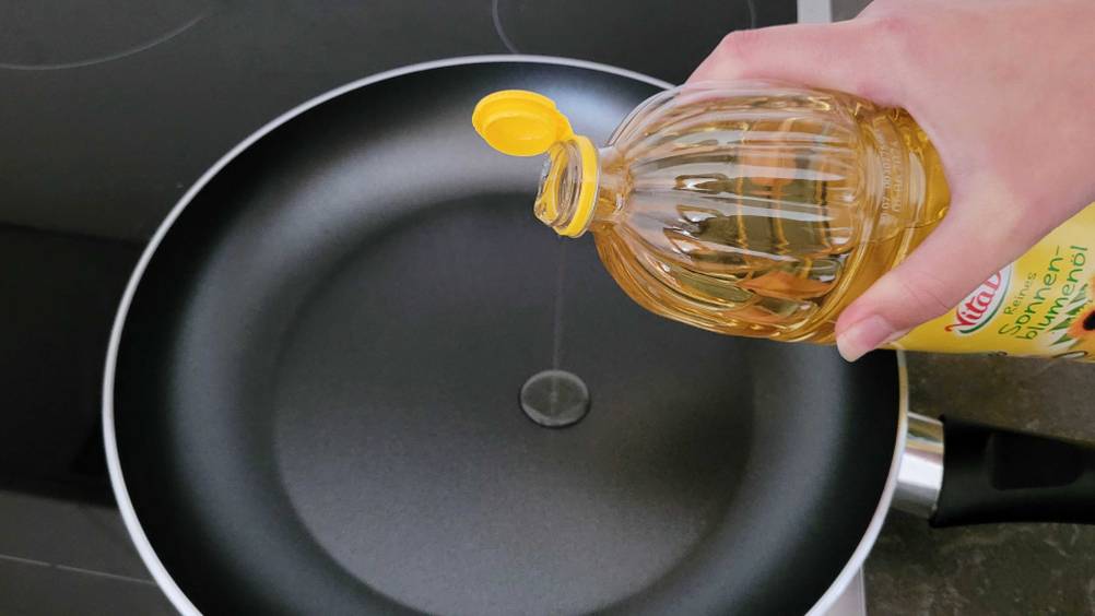 Öl zum Braten getestet: Eine Hand schüttet aus einer Flasche, Öl in eine Pfanne.