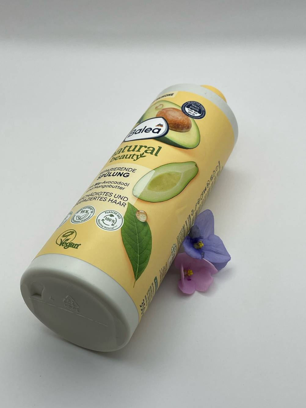 Die liegende Flasche des getesteten Haarbalsams liegt auf einer weißen Fläche, die mit Blumen verziert ist.