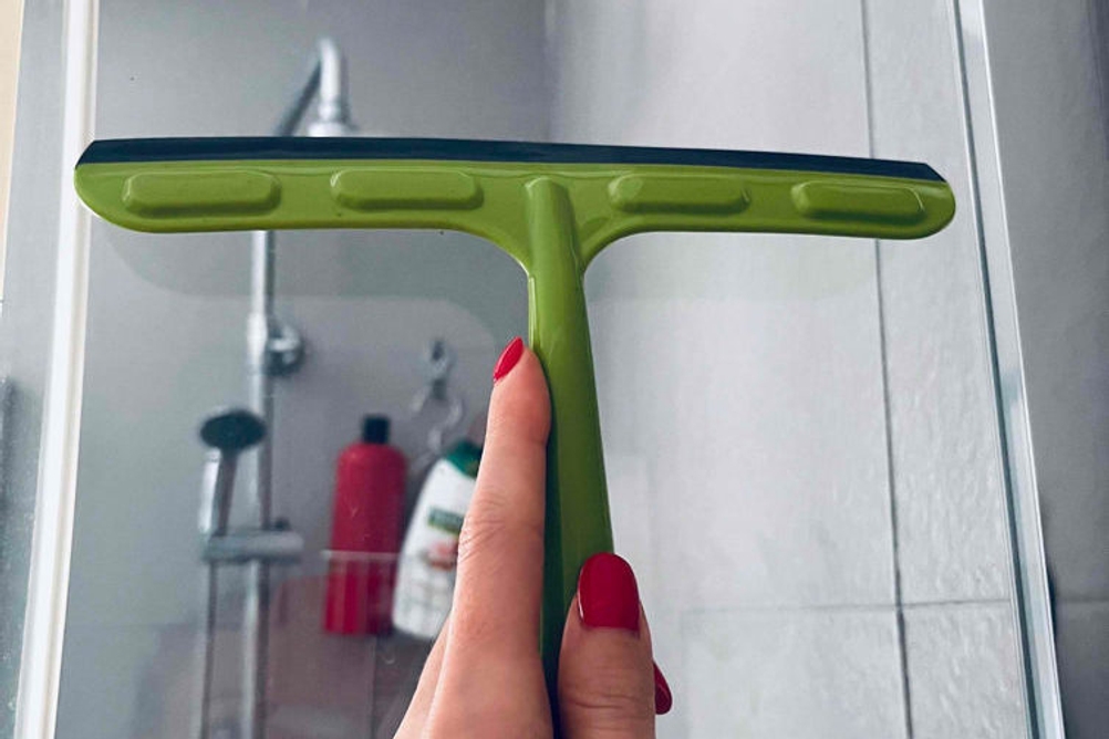 Fensterputzer im Test: Grüner Fensterputzer wird vor eine Duschwand gehalten.