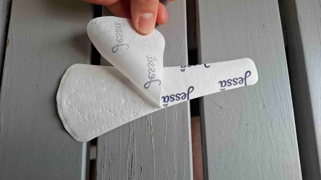 Eine Hand zieht an dem Klebeschutz von der Tanga-Slipeinlage im Test.
