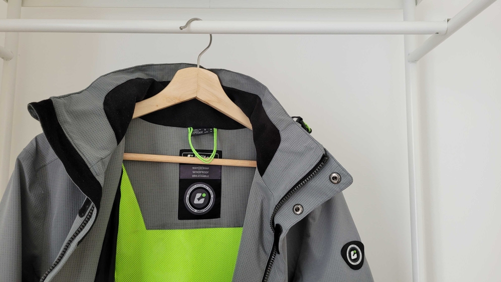 Herren-Regenjacke-Test: Eine Herren-Regenjacke der Marke Killtec hängt geöffnet auf einem Kleiderbügel in einem Metall-Gestell. 