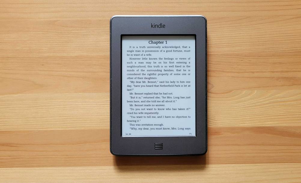 Auf einer Holzoberfläche liegt ein getesteter eBook-Reader mit Text im Display.
