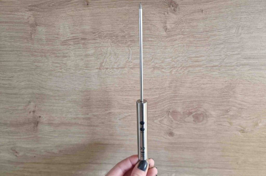 Eine Hand hält ein getestetes Küchenthermometer für Flüssigkeiten vor eine Holzfläche.