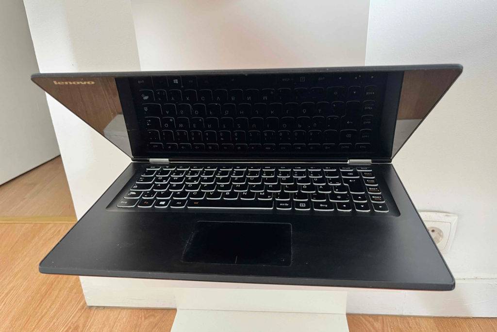 Lenovo Yoga im Test: Der Computer steht hab geöffnet von vorne auf einem weißen Regal