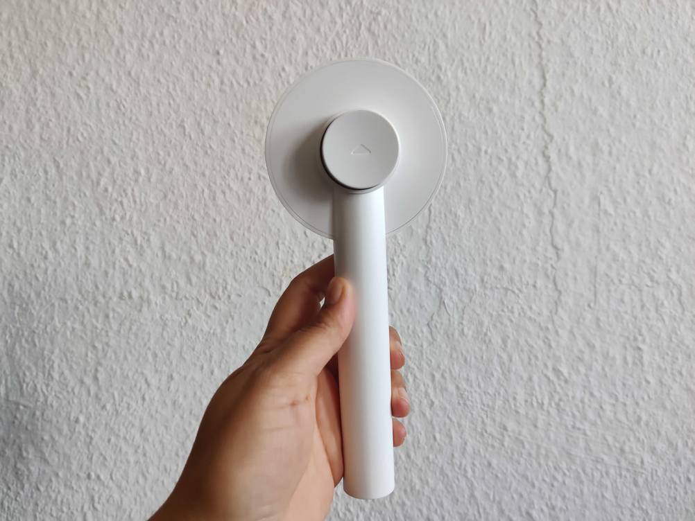 Im Test: Eine Hand hält eine Katzenbürste mit der Rückseite nach vorne vor eine weiße Wand.