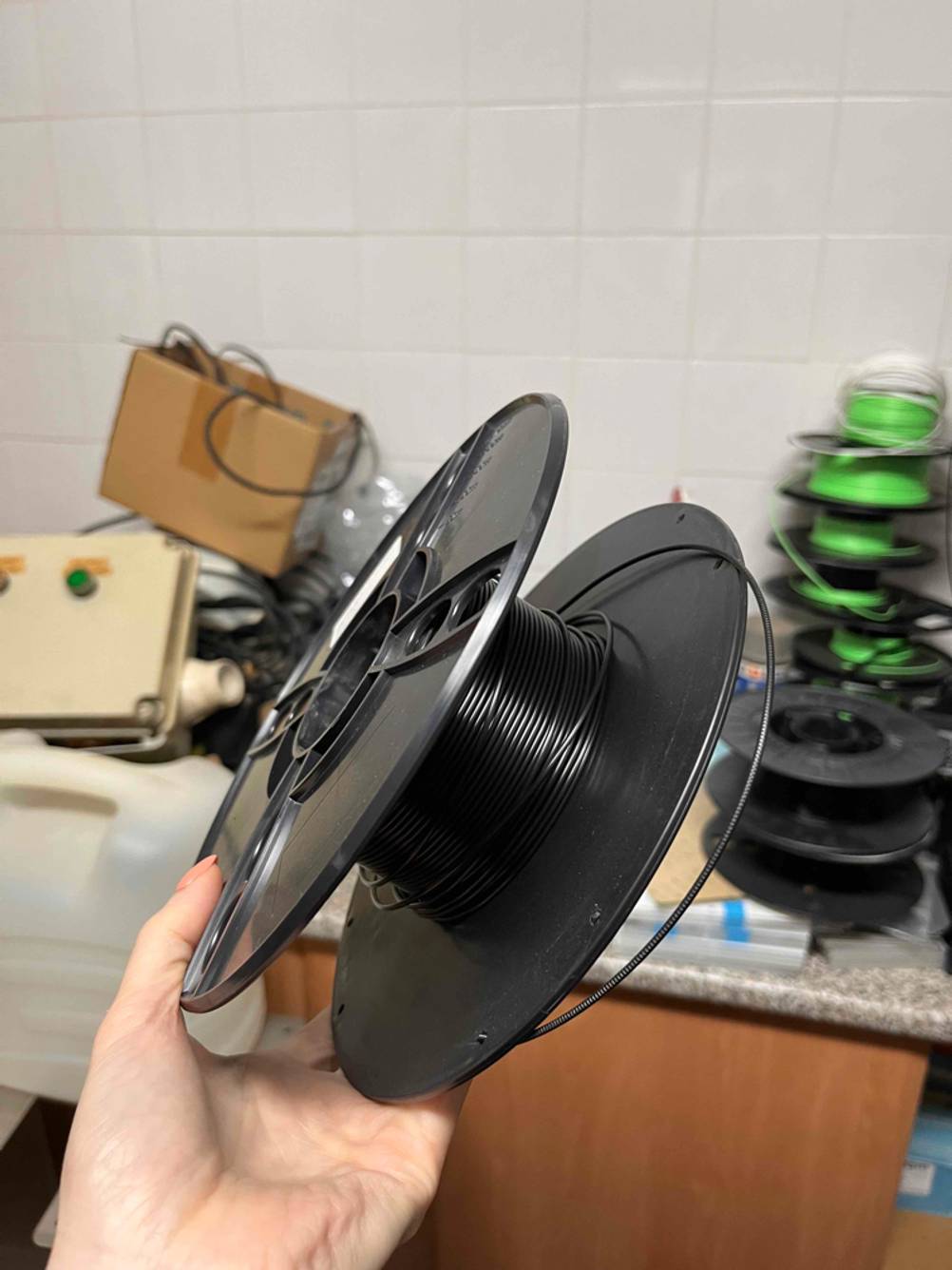 3D-Drucker-Filament getestet: Eine Hand hält eine Rolle mit schwarzem Filament vor eine Wand.