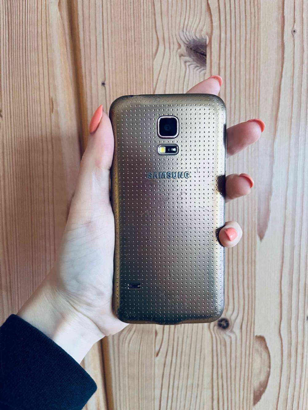 Kleine Smartphones getestet: Eine Hand hält ein Gerät mit der Rückseite nach vorne vor eine Holzwand.