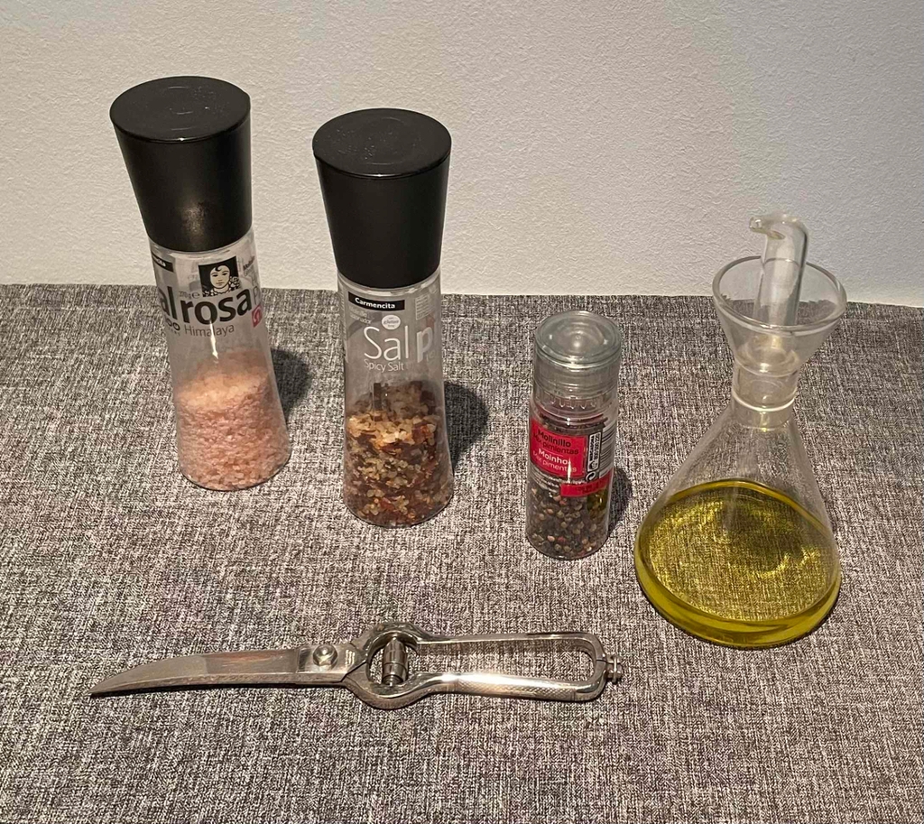 Geflügelschere im Test: Eine Schere liegt geschlossen auf einer grauen Tischdecke vor einer Ölkaraffe und drei Gewürzspendern.