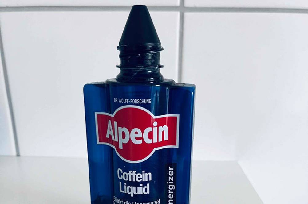Alpecin getestet: Eine geöffnete Flasche auf einer weißen Fläche im Vordergrund der Deckel.