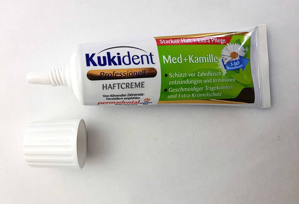 Die Tube mit der getesteten Haftcreme liegt geöffnet neben dem Verschluss.