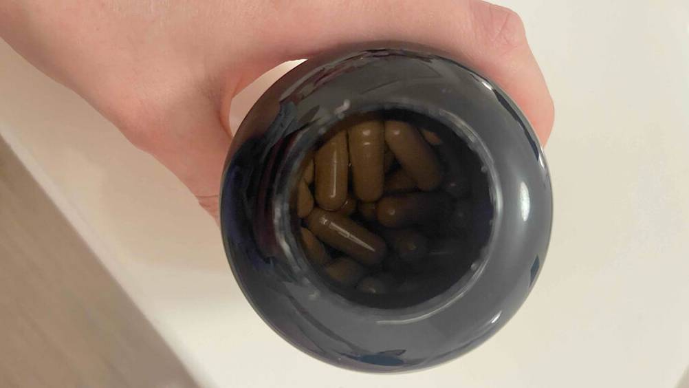 Eine Hand hält einen kleinen, lichtdichten, geöffneten Flakon in dem sich die getesteten Moringa-Kapseln befinden.