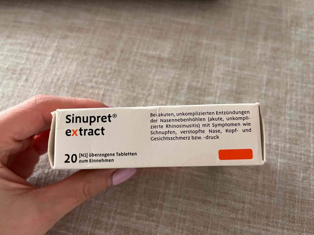 Eine Hand hält eine Packung des getesteten Schleimlösers seitlich vor eine helle Fläche.