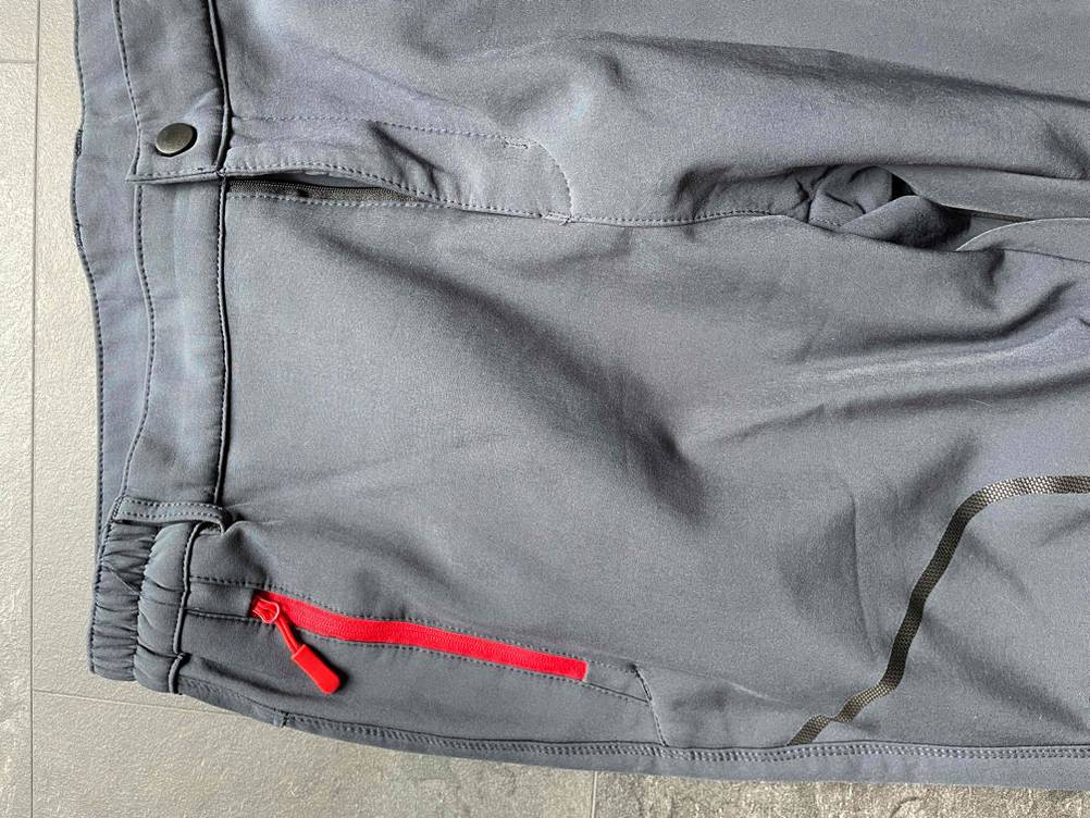 Softshellhose-Herren-Test: graue Softshellhose mit rotem Reißverschluss liegend auf einem Boden.