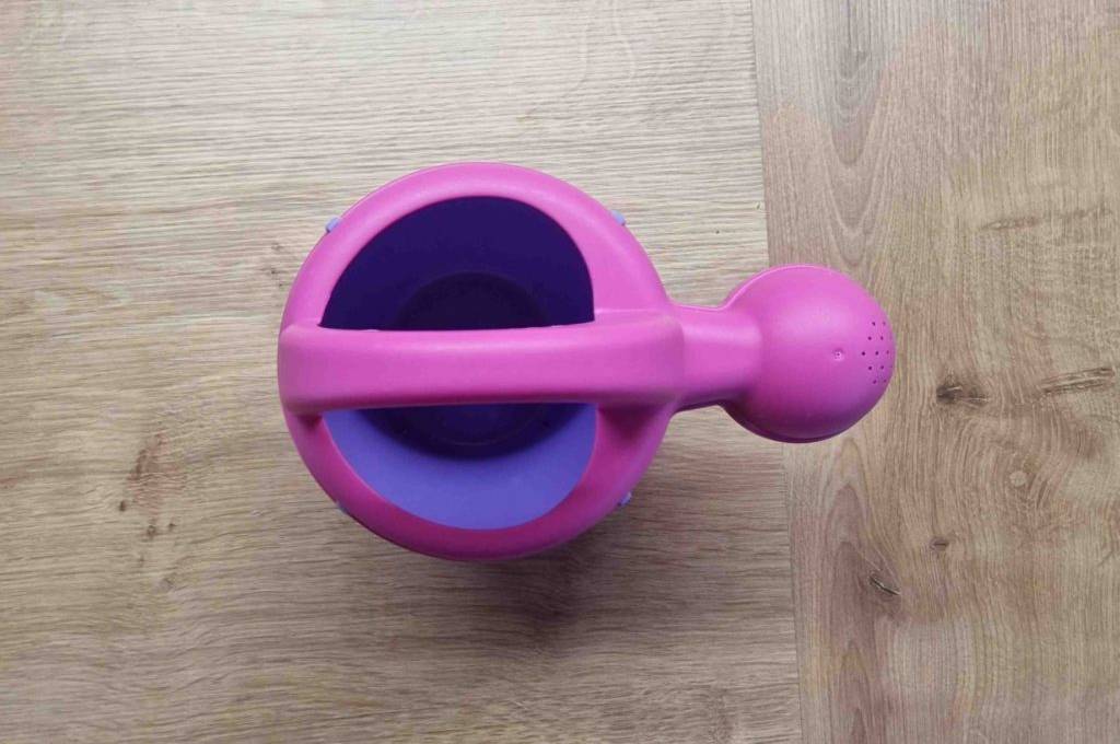 Wasserspielzeug-Test: eine lilafarbige Spielzeug-Gießkanne von oben - stehend auf einer Holzfläche.