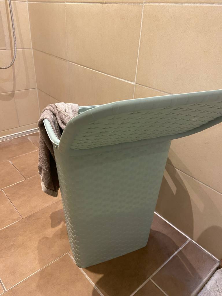 Der geöffnete getestete Wäschesammler inklusive eines beigefarbenen Handtuchs steht auf braunen Fliesen im Badezimmer.