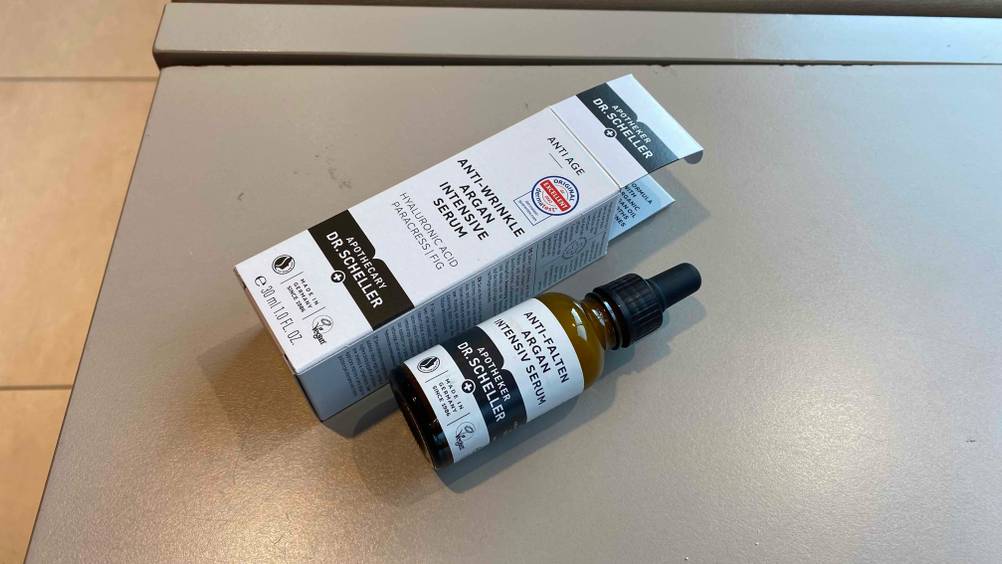 Anti-Falten Serum getestet: Ein Fläschchen neben seiner Verpackung auf einer beigen Fläche.