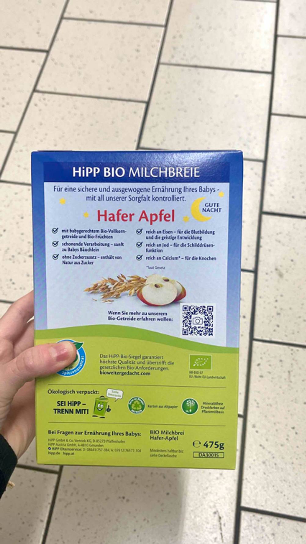 Der getestete Getreide-Obst-Brei von Hipp wird mit der Rückseite ersichtlich in der Hand gehalten.