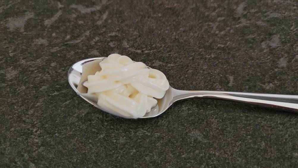 Die getestete Mayonnaise auf einem Löffel der auf einer dunklen Oberfläche liegt.